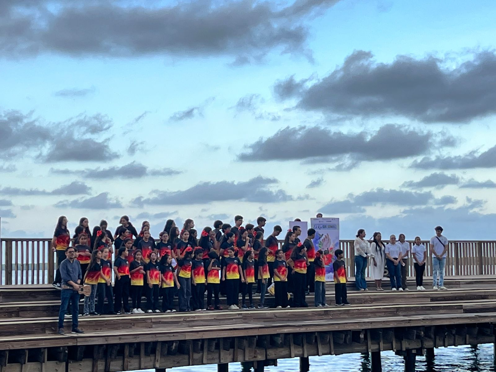 Coro estudiantil de El Río Que Somos cantando en el muelle al atardecer